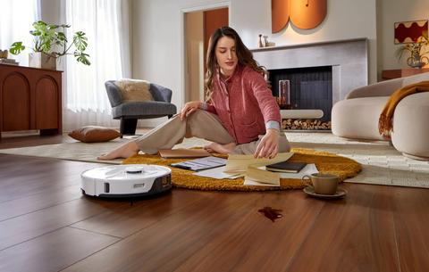 A woman is sitting on a wooden floor, while Roborock's smart vacuum cleaner is cleaning the floors and carpets.